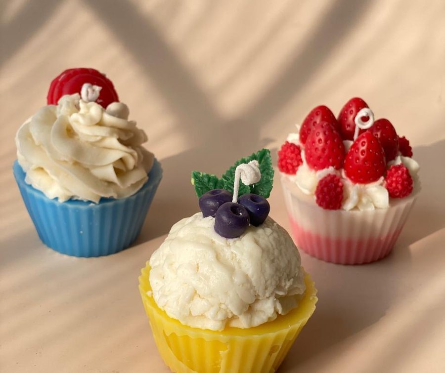 Three dessert candles shaped as cupcakes — whipped cream with a cherry, vanilla with blueberries, and one topped with strawberries.